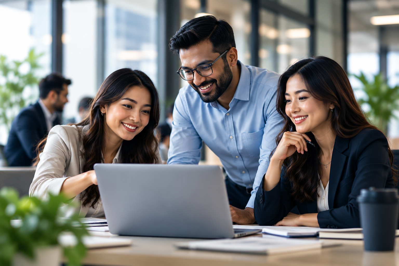 Three colleagues smiling while reviewing a profile together on a laptop
